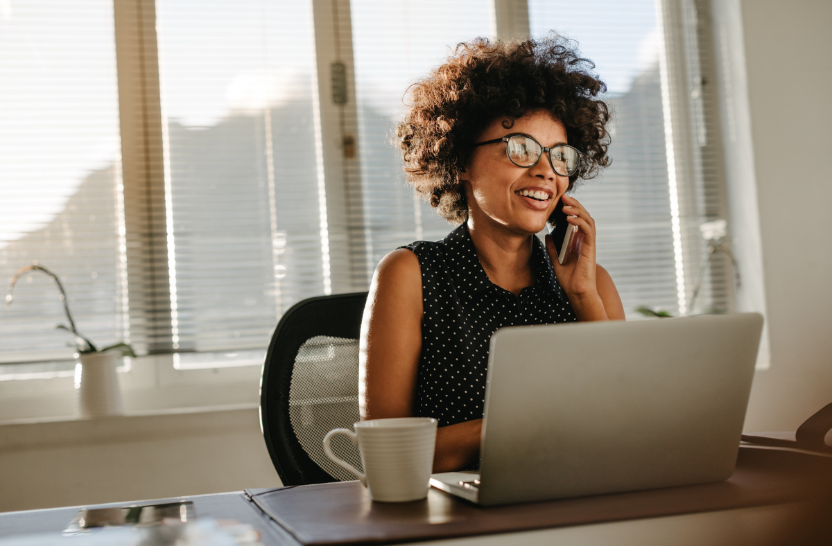 female sitting in office using laptop and phone to ear