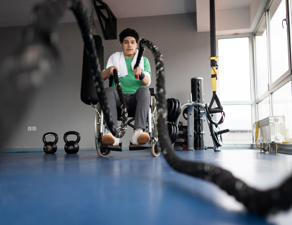 young adult man in wheelchair using ropes to workout in gym