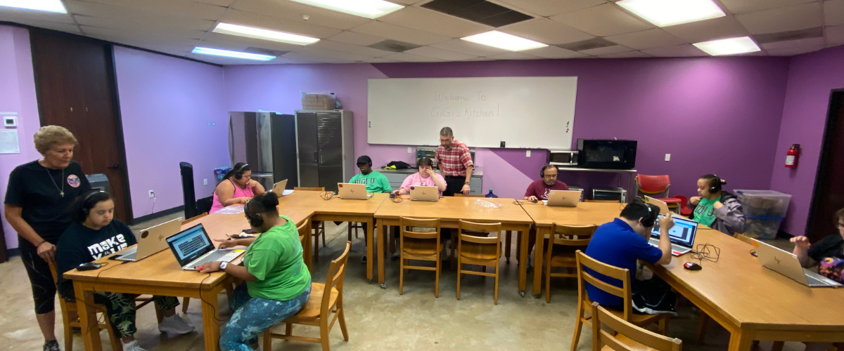 high school students sitting at table doing work on digital devices