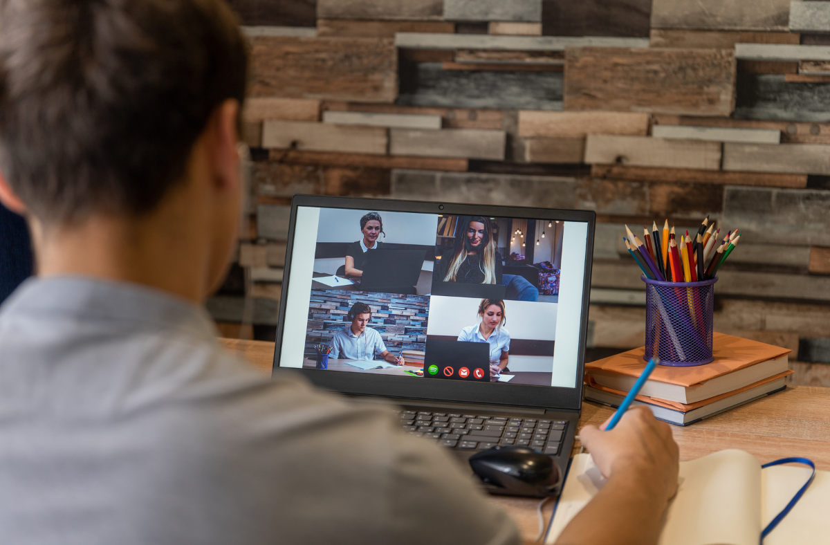 young man sitting at laptop on zoom call with 4 other business people