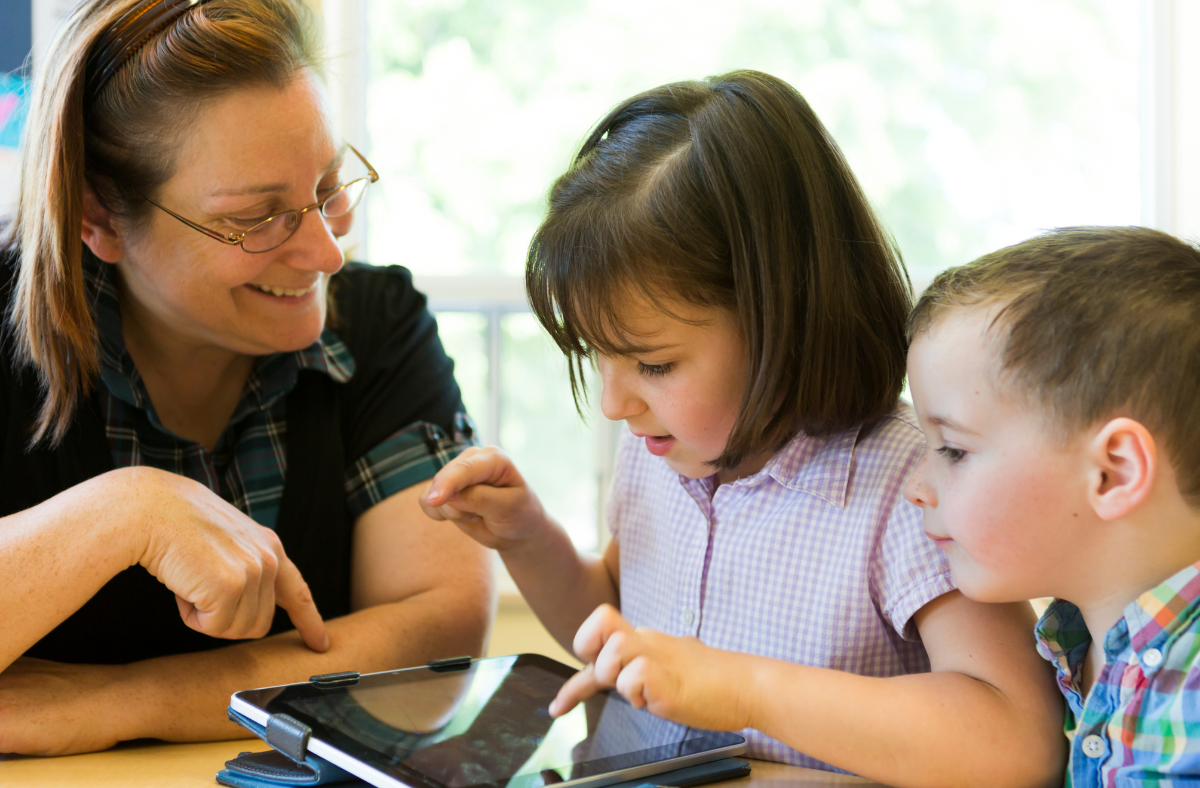 teacher helping two kids use ipad