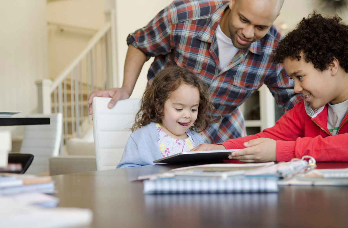 dad and older brother helping young girl communicate using ipad