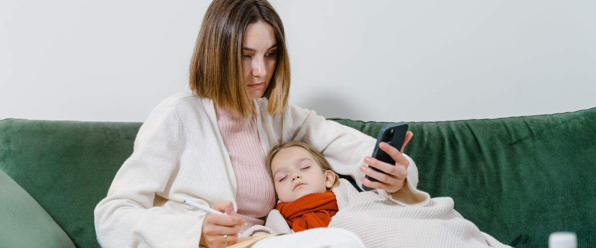 mom on couch looking at phone with sick child laying in her lap