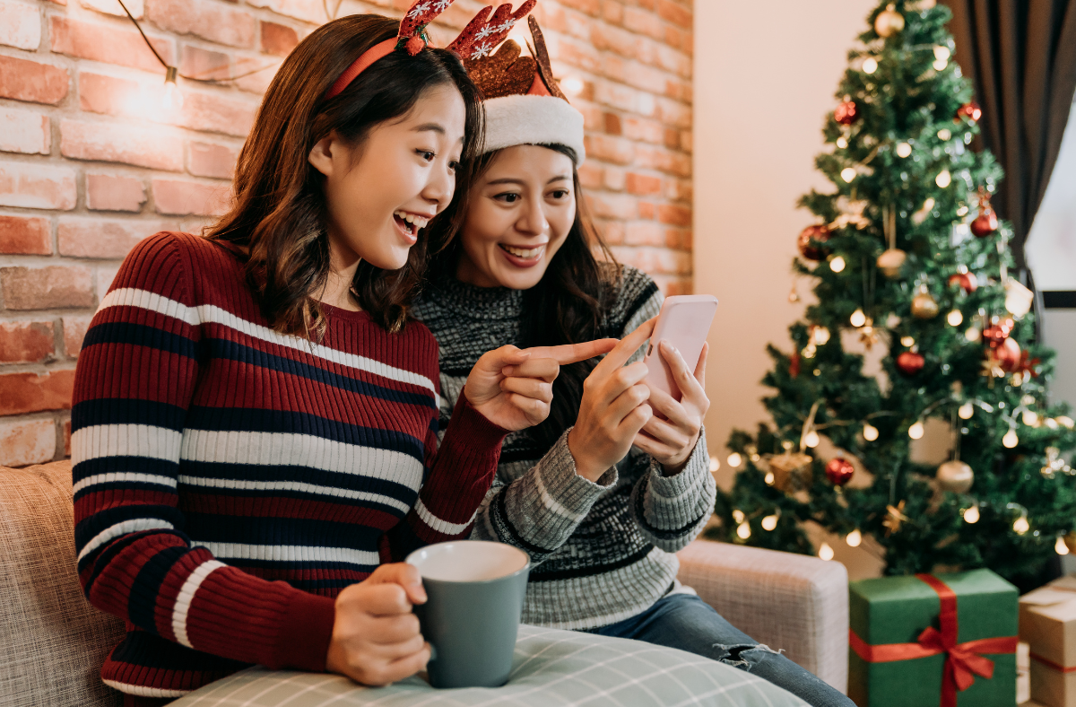 Two young ladies looking at phone together in front of Christmas tree
