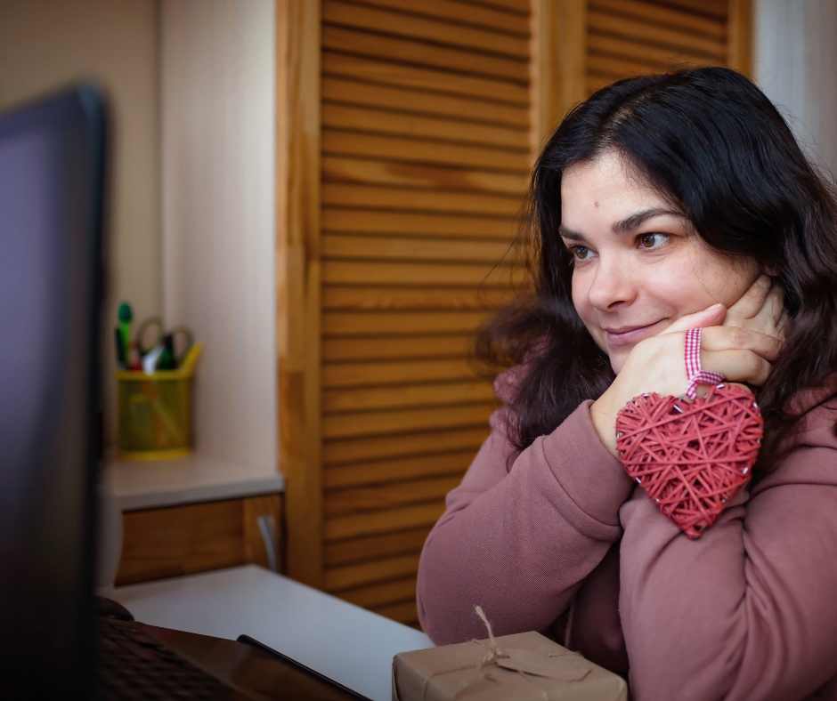 young woman holding heart ornament looking at computer screen