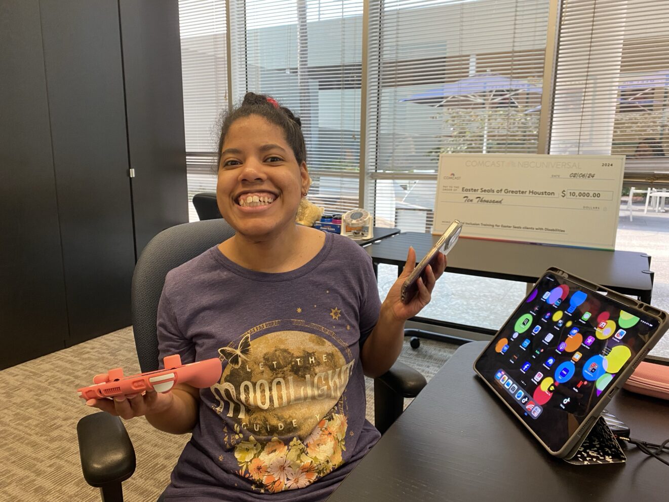 Malissa in AT lab with a device in each hand, and a monitor screen full of color and icons