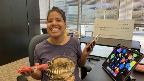 Malissa in AT lab with a device in each hand, and a monitor screen full of color and icons