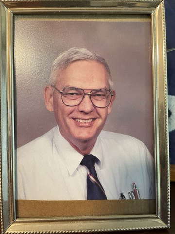 Portrait of Albert Swarts (gray-haired. clean-shaven white male with broad face, eyeglasses, and broad smile) in business shirt and necktie. Cluster of pens and pencils in his left breast pocket.