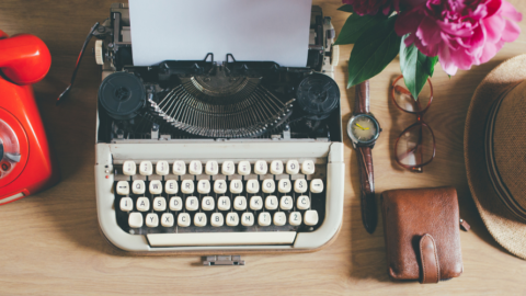 1980s typewriter and red telephone on desk with hat, wallet and glasses