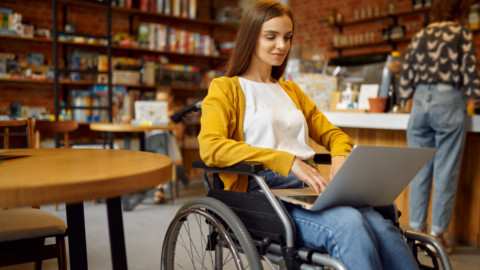 young adult woman in wheelchair using laptop in library