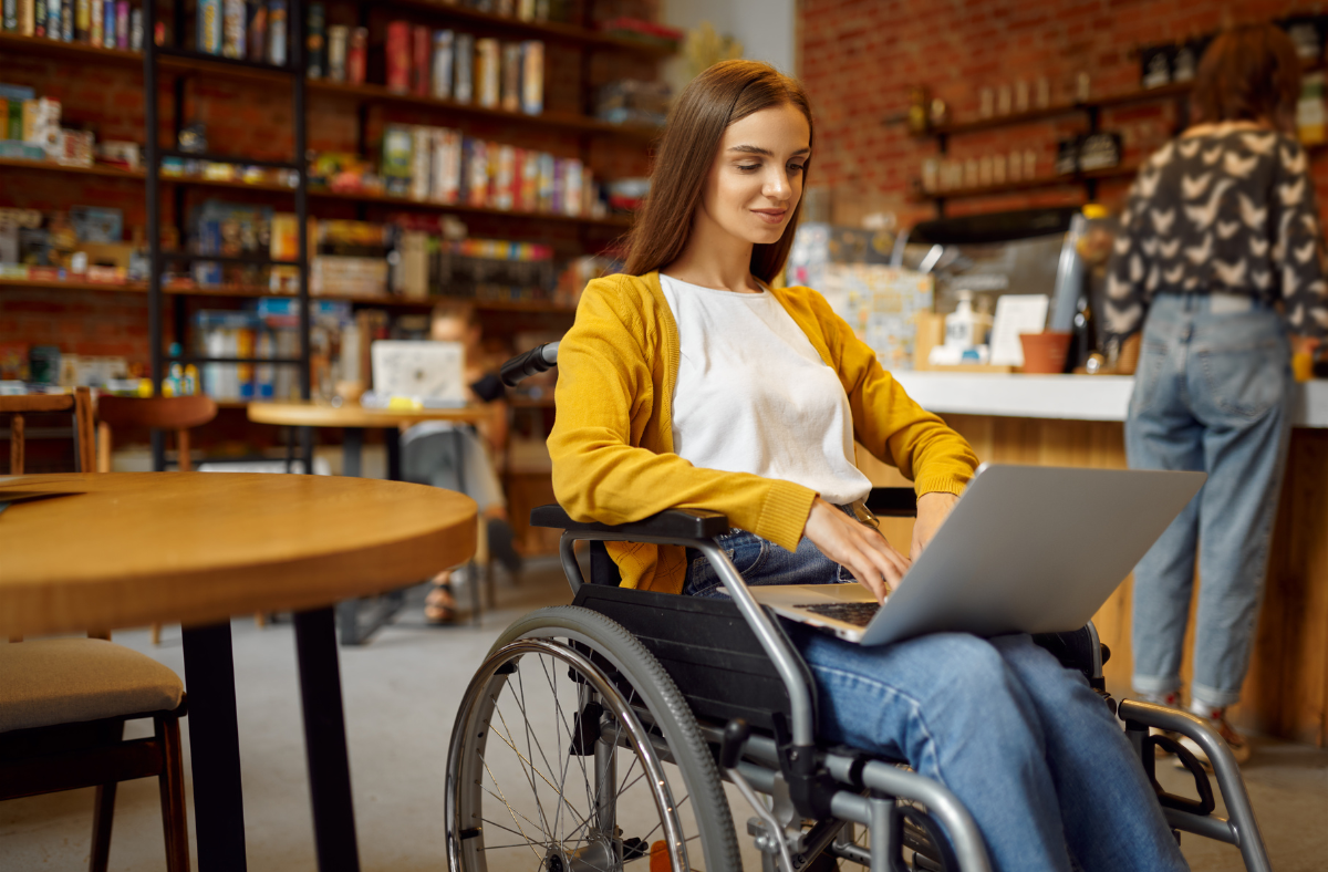 young adult woman in wheelchair using laptop in library