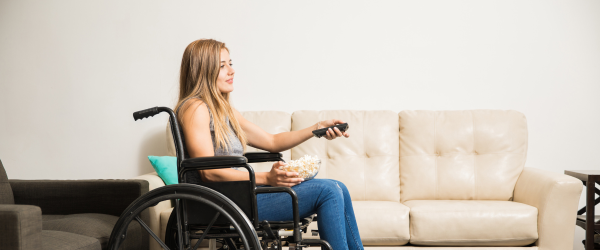 young adult woman sitting in wheelchair with bowl of popcorn on lap with tv remote in hand