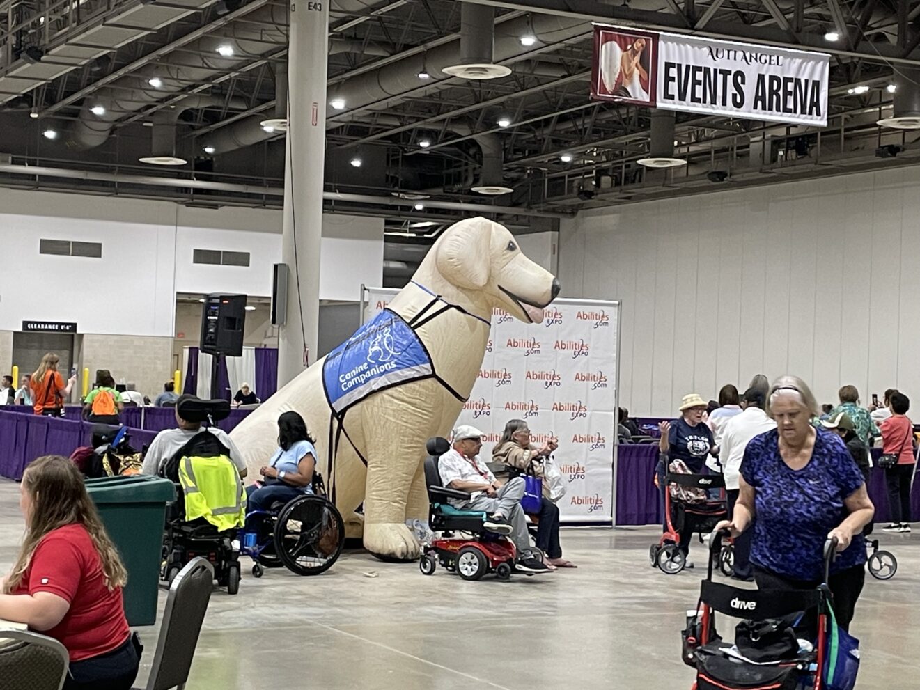 Giant "service dog" model from Canine Companions, right-profile view. Dog is white and floppy-eared with a blue "Canine Companions" vest.