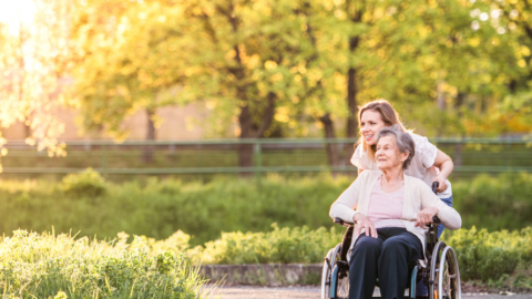 woman pushing older adult woman in wheelchair outside