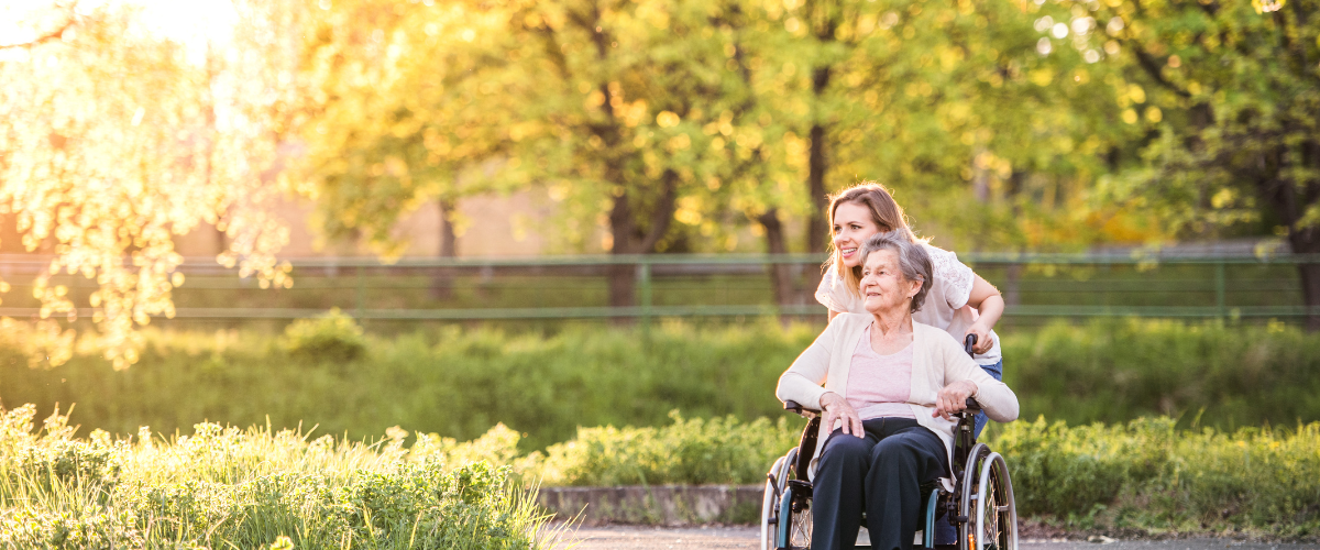 woman pushing older adult woman in wheelchair outside