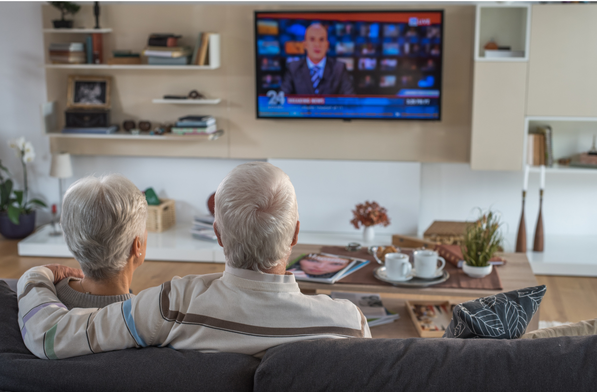 two older adults sitting on couch watching tv