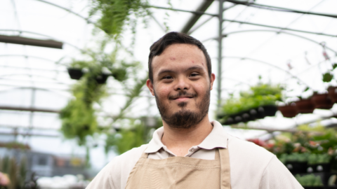 young man with down syndrome standing in green house
