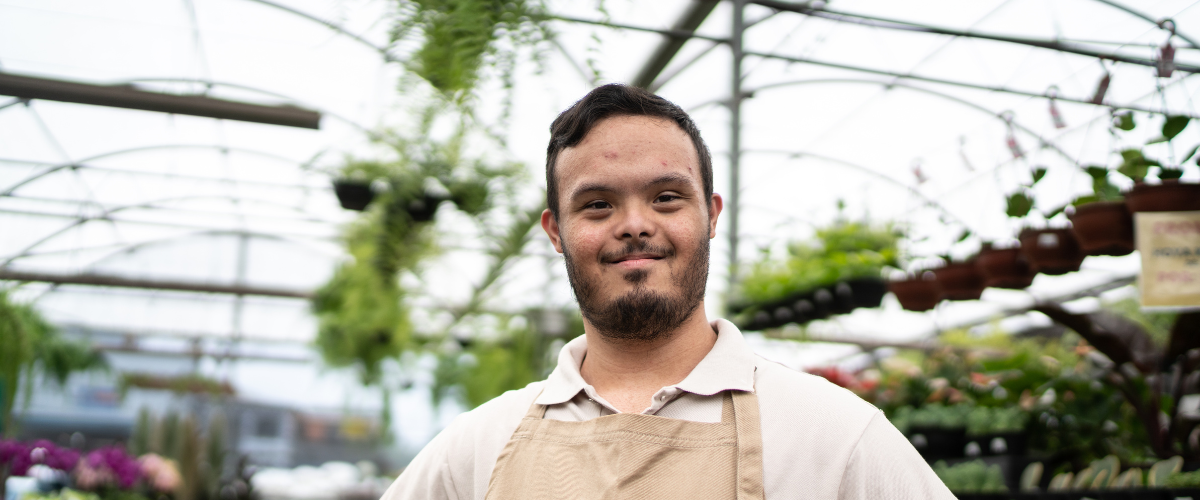young man with down syndrome standing in green house