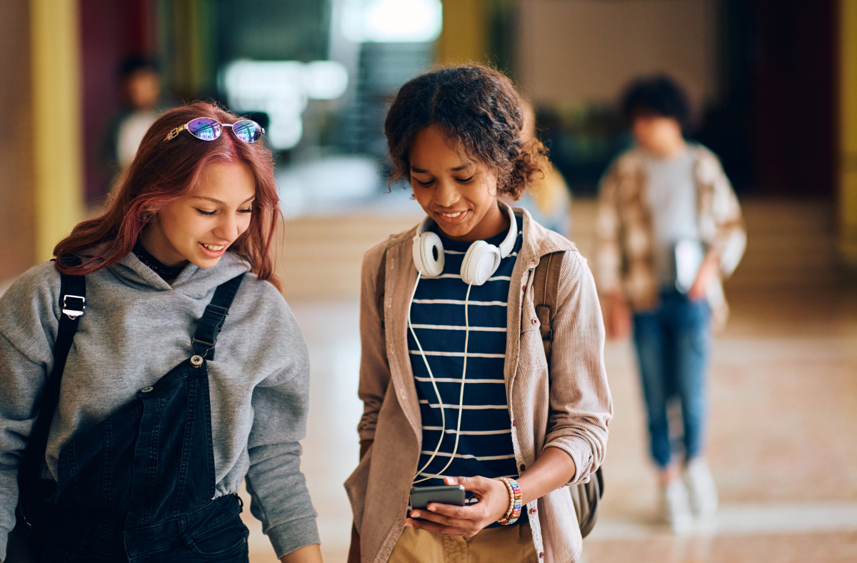 2 teen girls using phone in school hallway