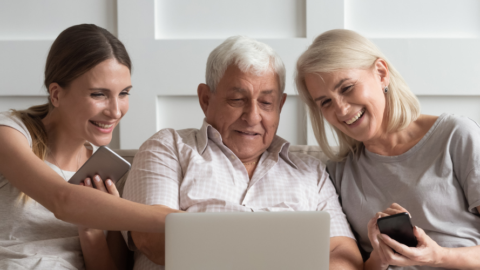 3 adults sitting on couch together looking at laptop