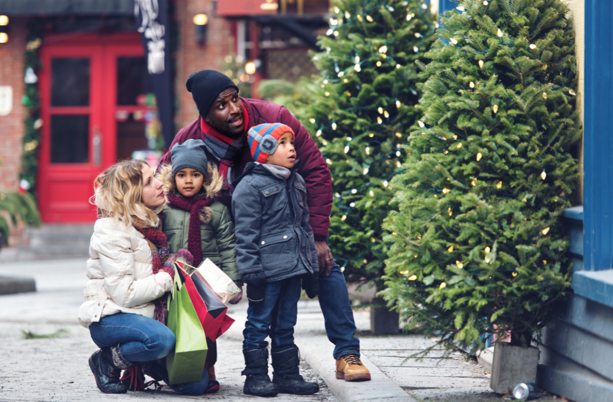family of 4 with 2 small children bundled up outside looking at Christmas tree lights