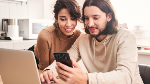 2 people sitting at table looking at laptop and phone