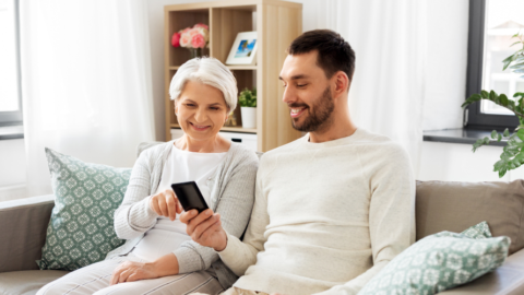 older adult holding smartphone with younger adult sitting next to her on couch looking on