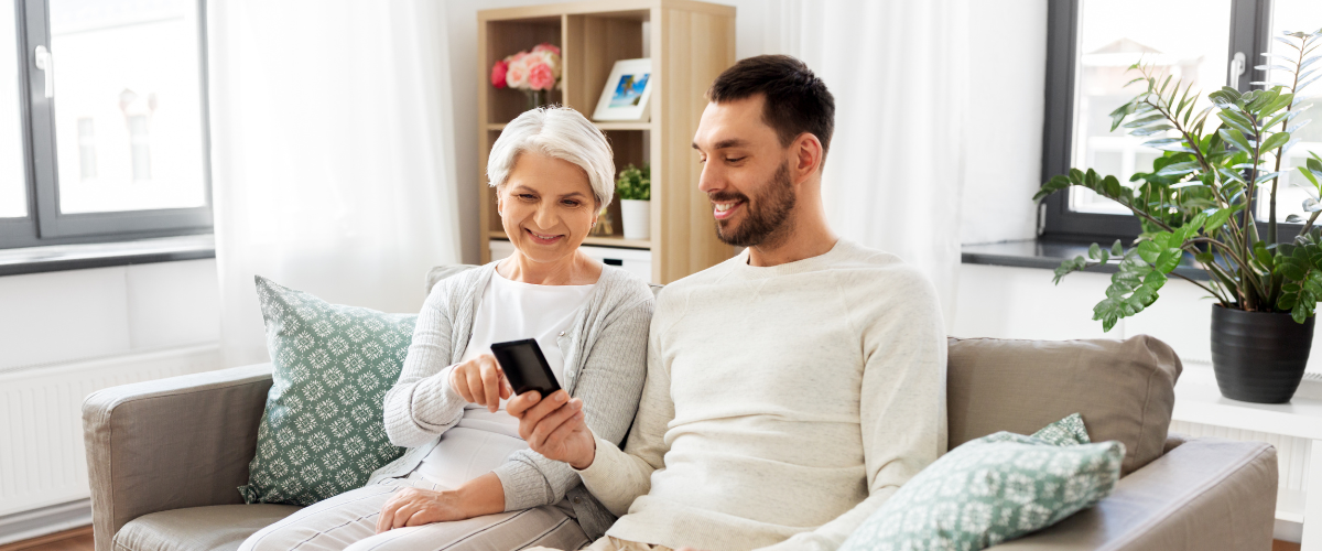 older adult holding smartphone with younger adult sitting next to her on couch looking on