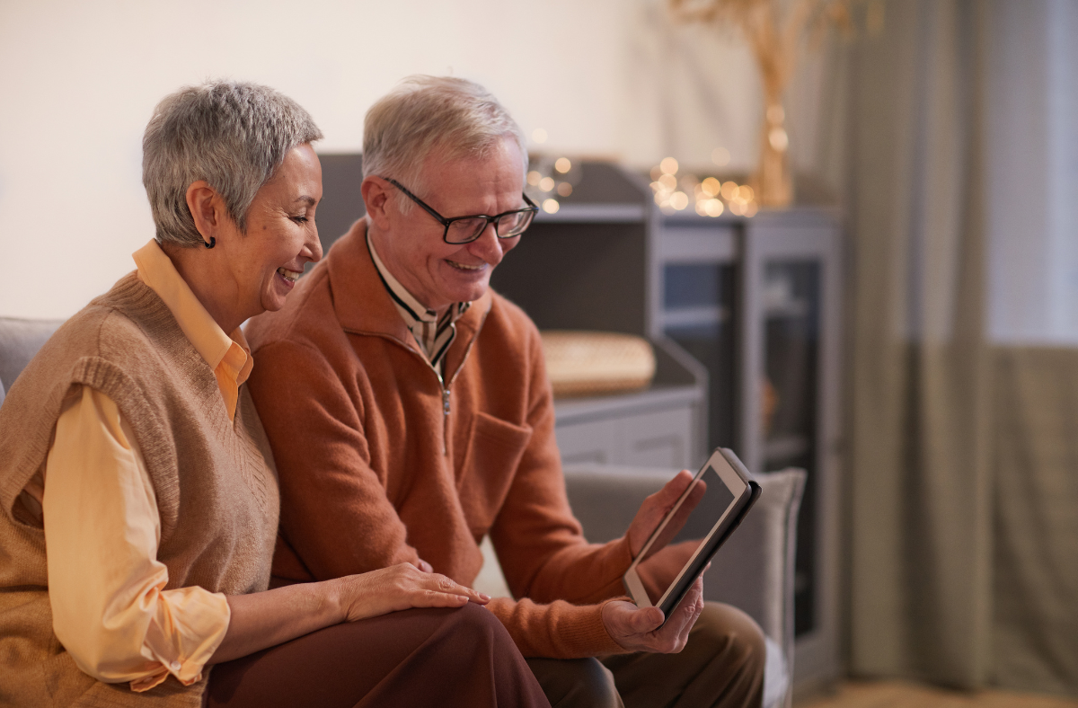 2 older adults sitting on couch together looking at tablet