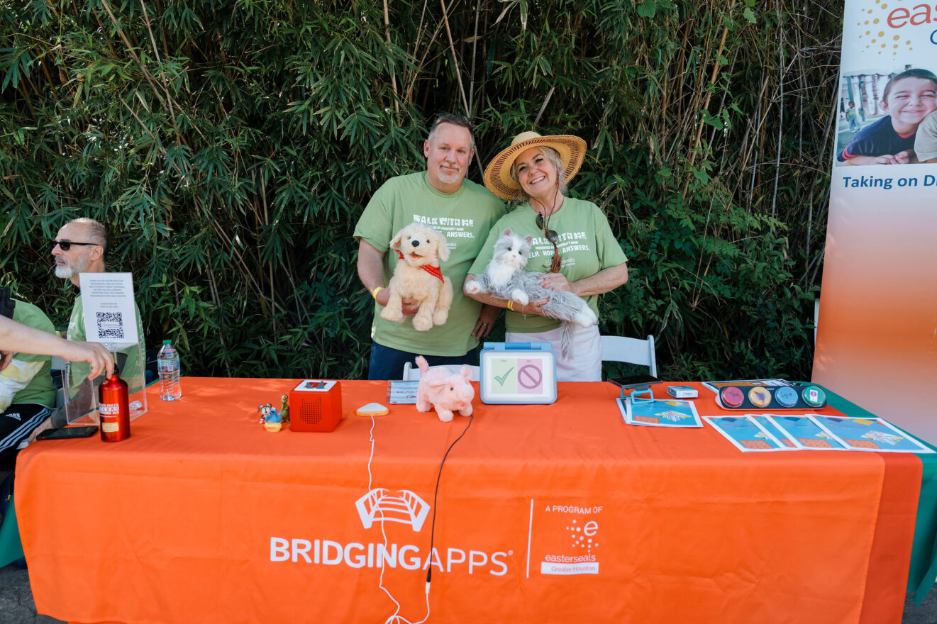 two adults holding a stuffed dog and cat smiling in front of table