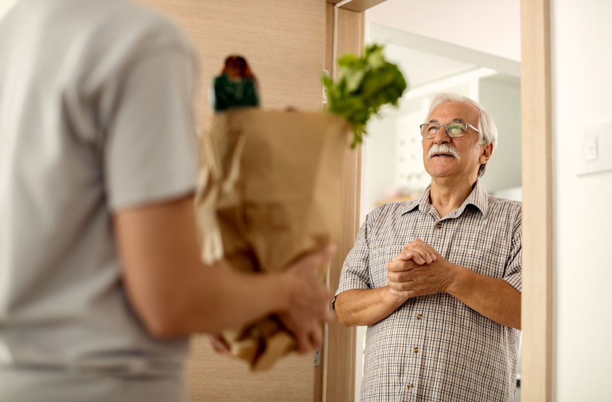 older man standing at door accepting grocery delivery order