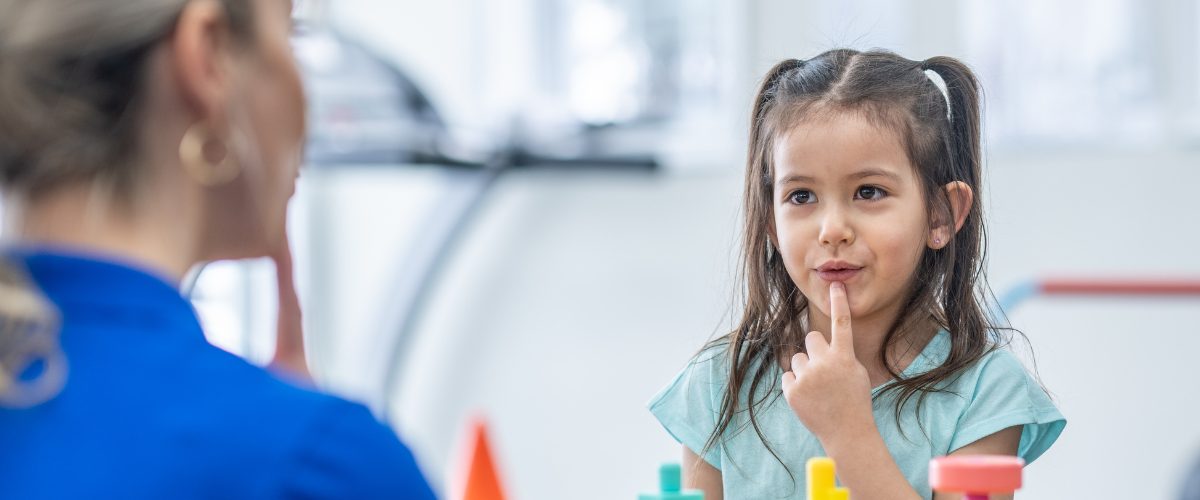girl pointing to mouth while looking at therapist's face