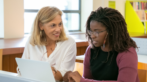 young adult sitting at computer being helped by teacher