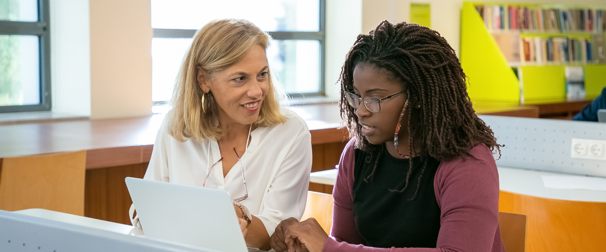 young adult sitting at computer being helped by teacher