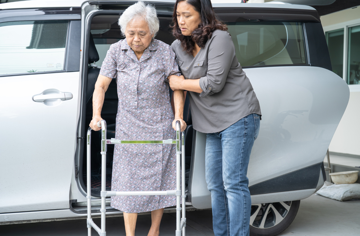 older adult woman with walker being assisted out of van