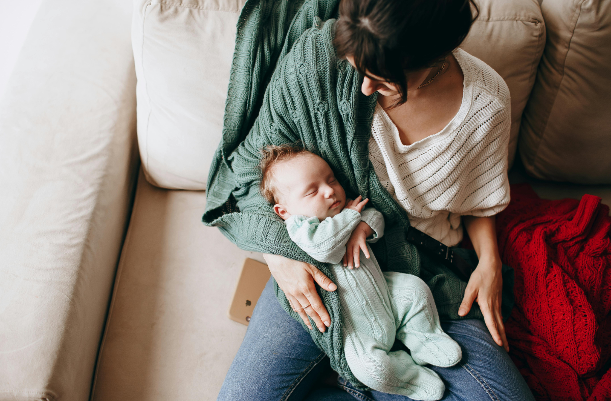 woman sitting on couch holding baby with iphone sitting beside her