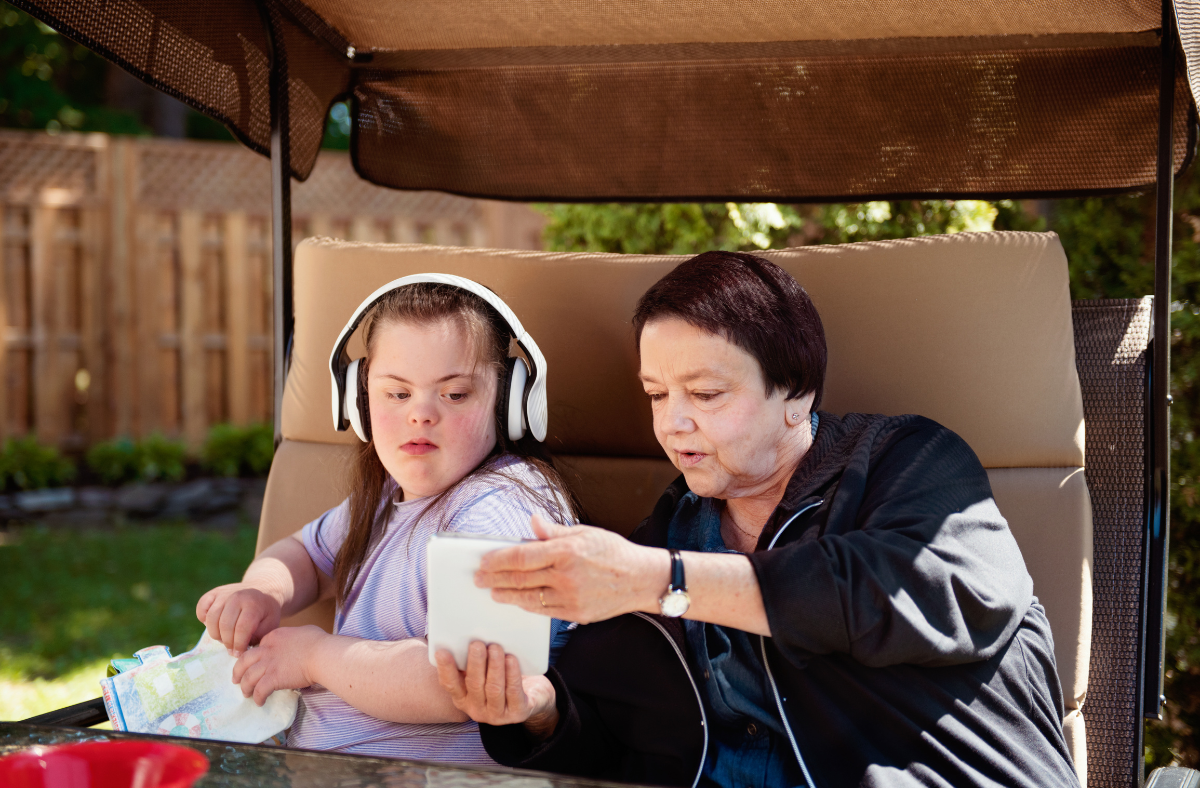 girl sitting with older adult woman, both looking at tablet device
