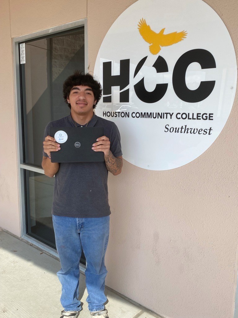 Student standing next to giant "HCC / Houston Community College Southwest" logo, holding up his new laptop.