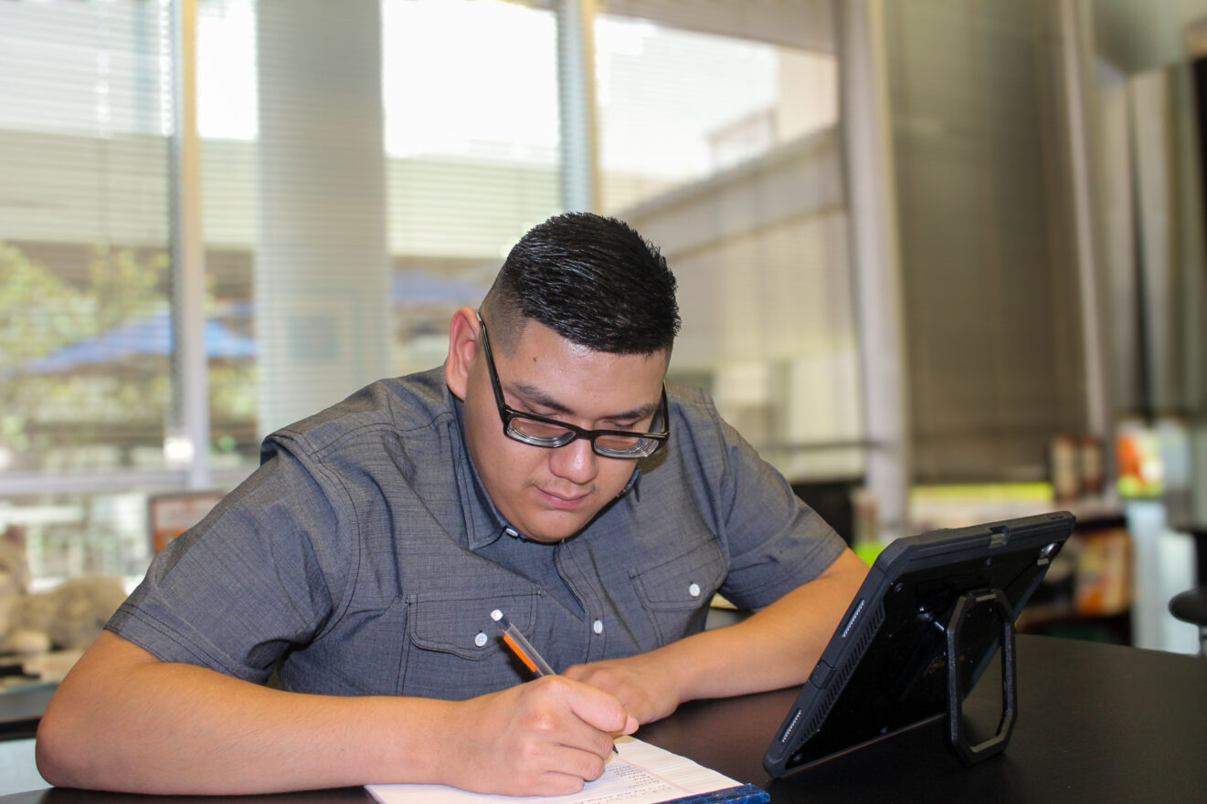 young adult guy looking down and writing on paper