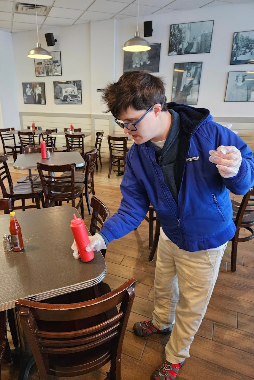 young adult guy wearing food safe gloves putting ketchup on a table