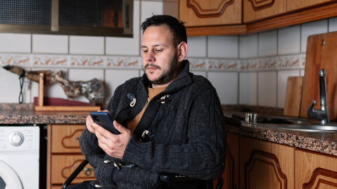 man in wheelchair in kitchen looking at phone in hand